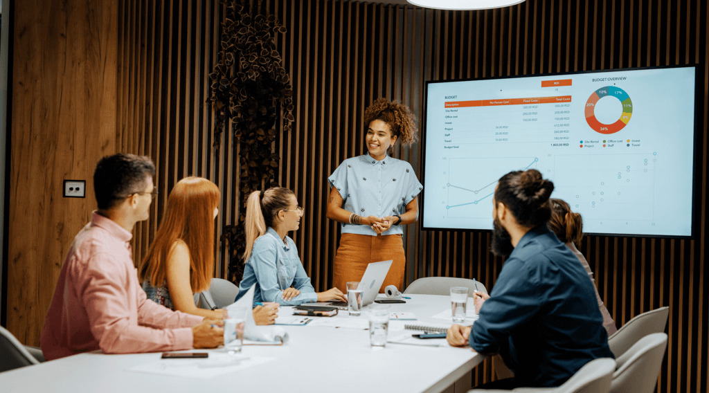 A group of people in a meeting room with a girl presenting