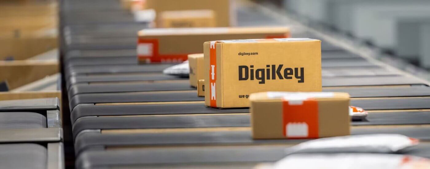Several DigiKey packages move along a conveyor belt in a warehouse, sparking a silent conversation of efficiency and innovation within the shipping facility.